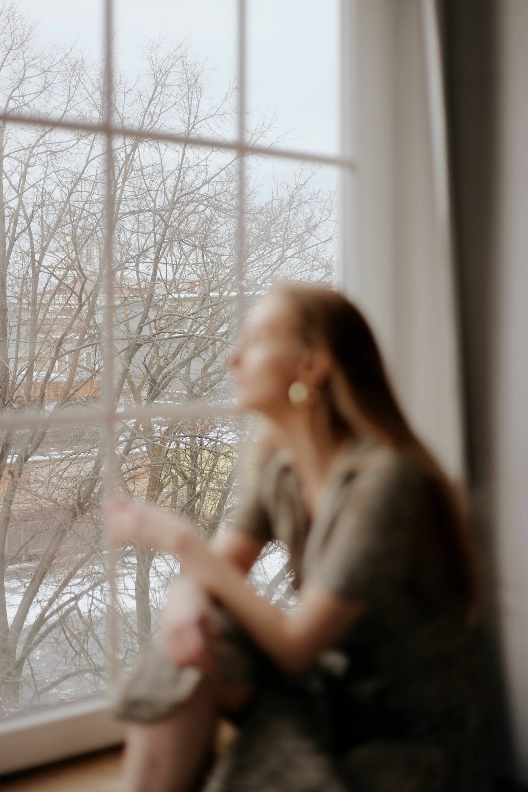 Femme assise près d’une fenêtre, dans une atmosphère calme et lumineuse.