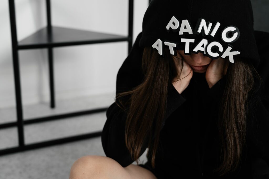 Femme anxieuse assise sous une capuche portant l’inscription Panic Attack